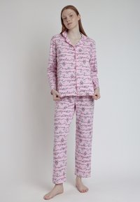 Conjunto de pijama rosa con mangas largas y pantalones, que presenta un patrón divertido de figuras y palabras en blanco y negro. Tela suave con una textura lisa.