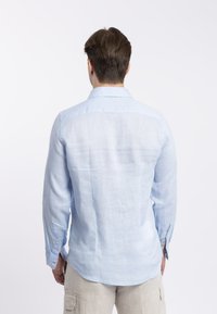 Camicia a maniche lunghe in lino azzurro chiaro, con colletto, polsini con bottoni e un tessuto liscio, leggermente strutturato. Vista dal retro.