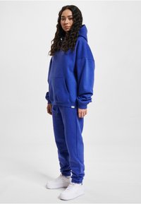 Blue sweatshirt and joggers set made from soft fabric; features a hood, front pocket, and elastic cuffs; paired with white sneakers.