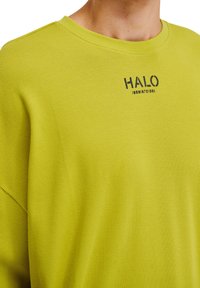 Limegrön långärmad skjorta i strukturerat tyg. Har en rund halsringning och ordet "HALO" tryckt i svart på bröstet.