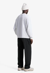 Biela košeľa s dlhým rukávom, čierne nohavice a krémové tenisky. Košeľa má okrúhly výstrih a čiapka je svetlá rebrovaná pletená. Neformálny dizajn.