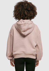 Lys rosa, oversized hettegenser med snor i hette, ribbestrikkede ermer og kant. Mykt materiale og avslappet passform gir komfort.