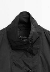 Czarna kurtka z wysokim kołnierzem zapinana na guziki z metką "Massimo Dutti" wewnątrz kołnierza, prezentowana na jednolitym tle.