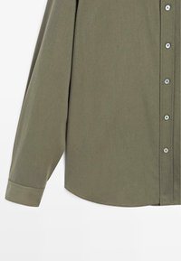 Camicia button-up verde oliva con maniche lunghe, caratterizzata da una texture liscia, orlo arrotondato e bottoni chiari lungo il davanti.