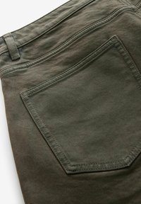 Olijfgroene denim broek met een gestructureerde afwerking, voorzien van een kenmerkende achterzak, versterkte stiksels en een recht gesneden ontwerp.