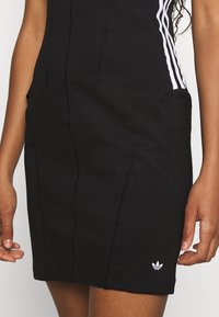 Black athletic dress with vertical seams, featuring white three-stripe accents along the sides and a small white logo at the hem.