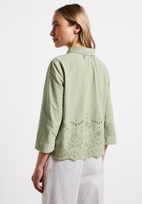 Blusa verde chiaro con colletto, maniche a 3/4 e design ricamato a intaglio all'orlo. Tessuto morbido con una superficie liscia.