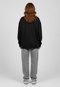 Felpa nera oversize con spalle basse, abbinata a pantaloni grigi chiari e sneakers bianche. Tessuto liscio, vestibilità rilassata.