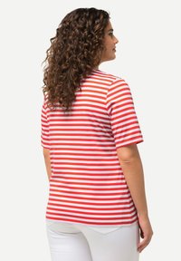 Camiseta de rayas rojas y blancas de manga corta, hecha de algodón, con un ajuste relajado, escote redondo y dobladillo recto, combinada con pantalones blancos.
