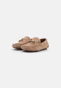 Beige suede loafers with stitched detailing, a front tassel, and gold-colored hardware accents; low-profile rubber sole for traction.