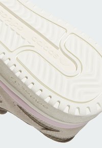 White sneaker sole with textured pattern, featuring a pink midsole, and embossed “adidas” logo visible. The design includes grooves for traction.