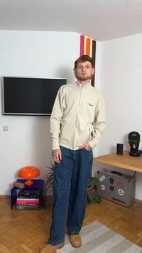 Bežna rebrasta jakna na zadrgo, modri široki kavbojki in bež škornji. Ozadje vključuje oranžno svetilko in manjšo mizo s knjigami.