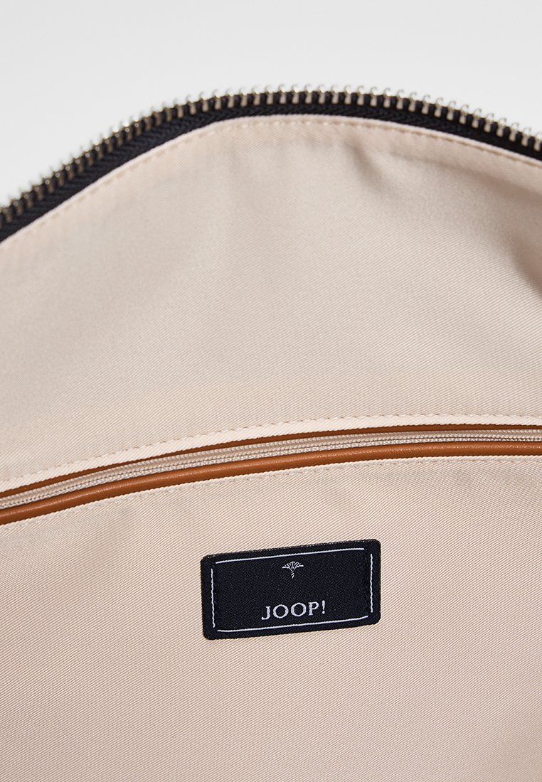 Beige Stoffinnenraum einer Tasche, mit einem hellbraunen Reißverschluss und einem schwarzen Etikett mit weißem Text "JOOP!" sowie dekorativer Naht.