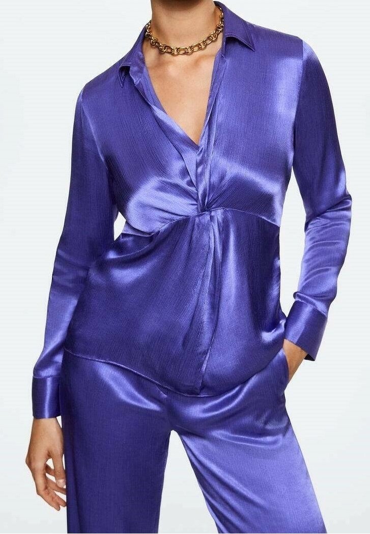 Blusa de satén morada con escote en V, detalle de torsión en la parte frontal y mangas largas. La tela tiene un acabado suave y brillante.
