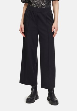Zwarte wijde broek met een hoge elastische tailleband, voorzien van op maat gemaakte plooien, gemaakt van een zachte stof. Gecombineerd met zwarte enkellaarsjes.