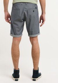 Pantaloni shorts grigi a motivo con risvolti, dotati di due tasche posteriori e di un'etichetta. Abbinati a scarpe scure, mostrano un design casual.