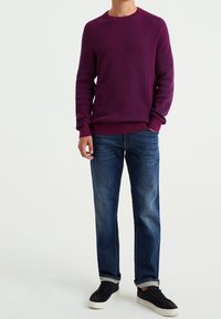 Suéter morado de canalé con escote redondo, combinado con jeans rectos azul y zapatillas de ante negras con suelas blancas.