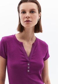 Lilla ribbet kortærmet top med V-hals og tre knaplukninger foran, med en glat kontrasterende kant.