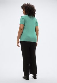 Žaliai balta dryžuota trumpomis rankovėmis marškinėliai, derinami su juodomis plačiomis kelnėmis. Marškinėliai turi aptemptą siluetą ir apvalų kaklo išpjovą.