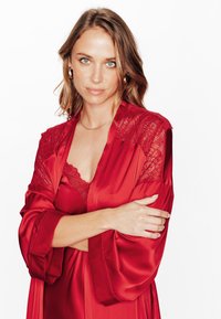 Accappatoio in raso rosso con dettagli in pizzo sulle spalle, scollo a V profondo e maniche fluide; elegante e dalla texture liscia con una leggera lucentezza.