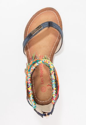 Platt sandal med marinblå rem och färgglad pärldetalj. Har en dämpad sula och en brun strukturerad sula.