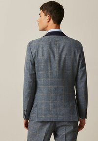 Veste de costume pour homme en bleu avec un motif à carreaux, dotée d'un col cranté et d'un tissu texturé. La vue de dos montre une coupe ajustée et une structure.