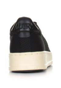 Sneaker nera con tomaia in tessuto strutturato e suola in gomma bianca vista da dietro, che mette in evidenza il pannello imbottito del tallone e i dettagli della suola.