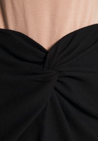 Tissu noir avec un détail noué au centre, superposé à un tissu nude doux. Les textures sont lisses et invitantes.