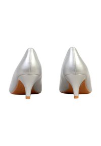 Paire de chaussures à talons hauts métalliques argentés vues de dos, présentant des talons pointus et des semelles couleur marron clair sur un fond blanc.