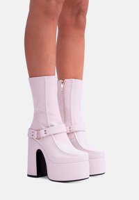 Stivali platform rosa con finitura lucida, tacco a blocco alto, chiusura con zip e una fascia con un dettaglio circolare. Design testurizzato.