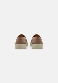 Pruunist nahast slip-on kingad ümmarguse varbaga ja heledast beežist kummist tallaga, millel on nõrk logo kandadel.