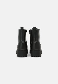 Botas de cuero negras hasta el tobillo con cremalleras a juego, suela gruesa y texturizada, y una silueta elegante. Sin adornos ni acentos visibles.