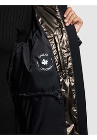 Crni kaput s sjajnom brončanom podstavom, s logotipom na unutarnjem džepu, rukavima od rebrastog pletiva i kopčama na dugmad. Vučna vrpca na rubu.