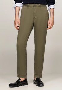 Pantaloni verde oliva in misto cotone con vestibilità slim. Presentano una chiusura con bottone e tasche classiche. Abbinati a mocassini neri.