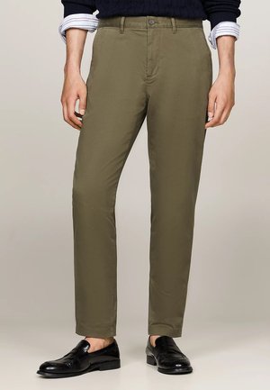 Pantaloni verde oliva in misto cotone con vestibilità slim. Presentano una chiusura con bottone e tasche classiche. Abbinati a mocassini neri.