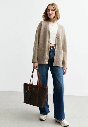 Cardigan marron clair avec des poignets côtelés, des boutons et des poches. Porté par-dessus un crop top blanc et associé à un jean bleu ample et un sac fourre-tout marron.