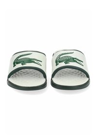 Sandalias de slide blancas con una superficie texturizada y un logo de cocodrilo verde. Presentan un diseño de tiras abiertas y acentos en verde oscuro alrededor de la suela.