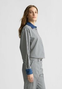 Gepunktetes, kurzärmeliges Hemd und Hose in Marineblau und Weiß mit einem Kragen und Manschetten aus Denimblau. Lange Ärmel, taillierte Passform, glatte Textur.