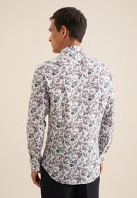 Langarmhemd aus weißem Stoff mit einem bunten Blumenmuster in Blau-, Rot- und Grüntönen; abgerundeter Saum, klassischer Kragen.