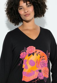 Czarna koszula z długim rękawem, z żywym pomarańczowo-różowym nadrukiem czaszki ozdobionej kwiatowymi akcentami. Dekolt w serek i miękka faktura materiału.