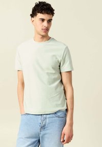 Ljusgrön bomulls-t-shirt med rund hals, korta ärmar och en avslappnad passform. Har en slät yta och en subtil horisontell mönstring.
