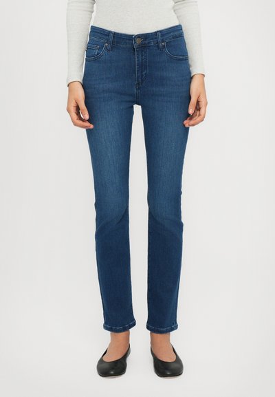 Sötétkék farmernadrág slim fit szabással, középmagas derékkal, elülső zsebekkel és klasszikus gombzárral. Simább textúra és egyenes szár.