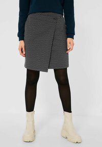 Zwart-wit gemusterde wikkelrok met een zijknopsluiting, gecombineerd met zwarte maillot en beige enkelboots met een chunky zool.