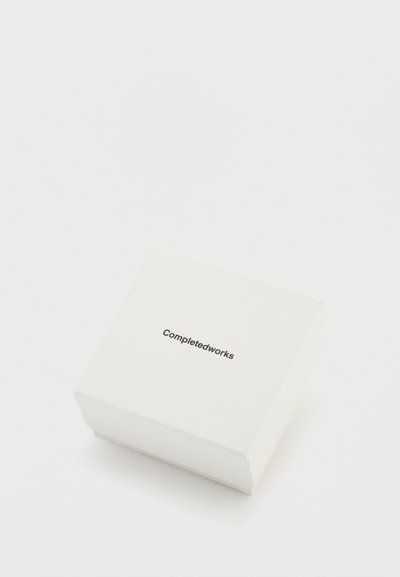 Biely papierový box s minimalistickým dizajnom. Na prednej strane je vytlačený text „Completedworks“ moderne bezpatkovým písmom.