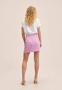 Gonna mini rosa con un design geometrico, abbinata a una maglietta bianca larga. La gonna presenta una forma aderente e una texture liscia.