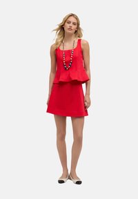 Rode mouwloze jurk met een peplumontwerp en een uitlopende rok. Gecombineerd met een kralenketting en bicolor flats. Soepele stofstructuur.