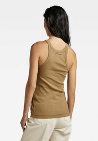 Top a coste color sabbia con design racerback. Presenta un logo discreto stampato sul retro. Abbinato a pantaloni larghi di colore chiaro.