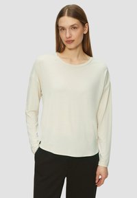 Crème langemouwen shirt met een ronde hals, losse pasvorm en zachte textuur. Opvallende drop shoulders en een gebogen zoom voor extra comfort.