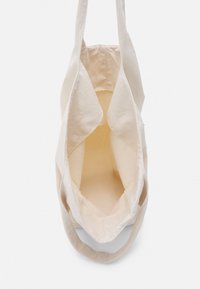 Beżowa torba płócienna z otwartą górą i szerokimi uchwytami, przedstawiona pusta z góry na białym tle.