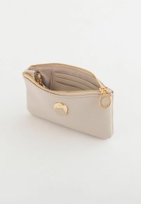Sac en cuir beige avec une fermeture éclair, doté d'un bouton rond doré et de fentes pour cartes à l'intérieur. Texture lisse, design compact.